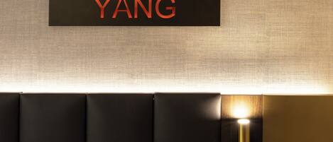 A hotel room with a black headboard, a wall-mounted sign reading "YANG", and a wall-mounted light fixture.