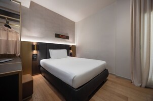 Una camera d'albergo moderna con un letto rifatto, un comodino con una lampada, un armadio e un cartello sopra il letto con la scritta PATH.