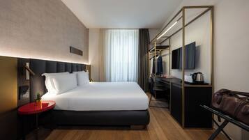 Una habitación de hotel moderna con una cama grande, un escritorio, un televisor y un bolso de cuero.