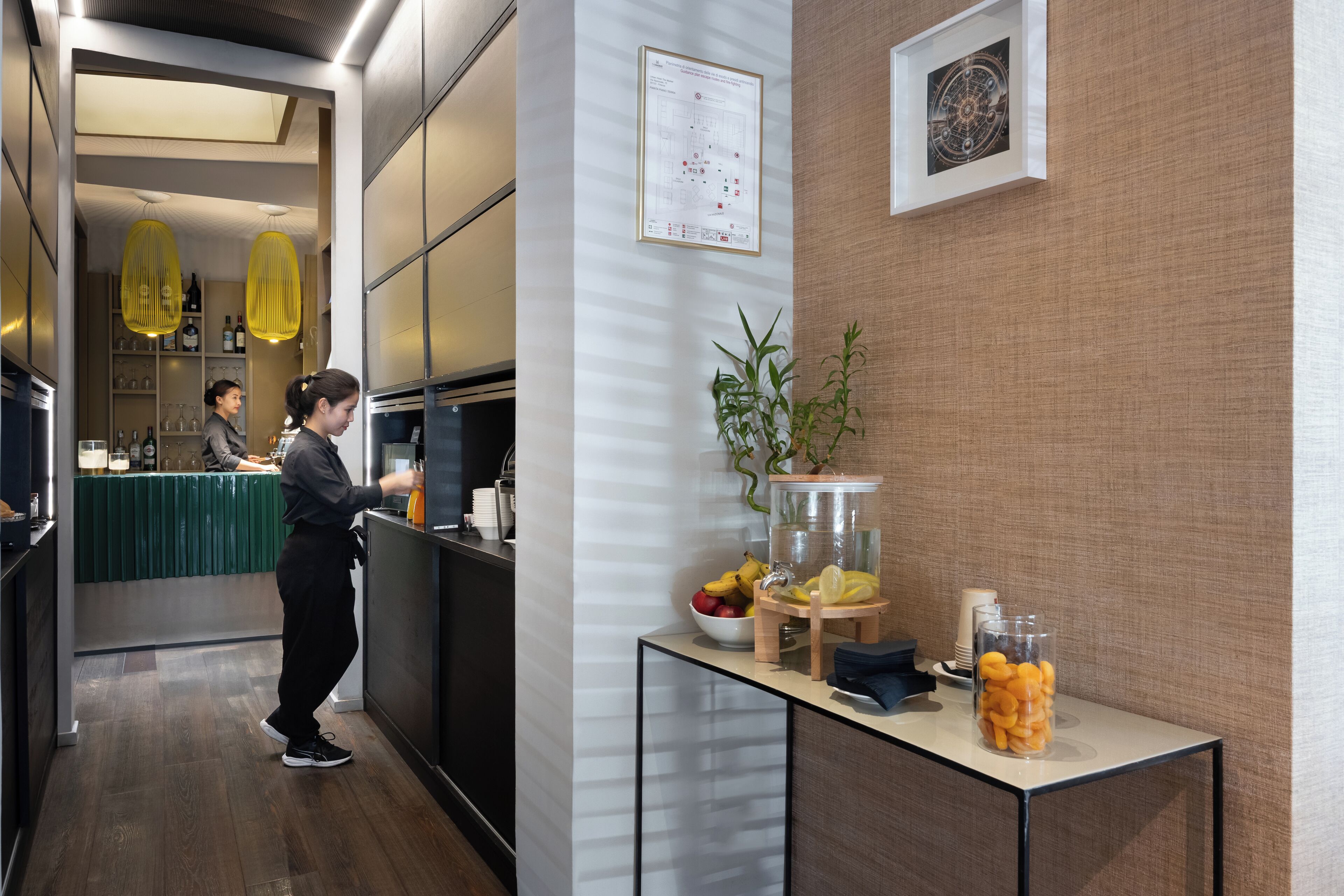 Un hall d’hôtel moderne comprenant un comptoir d’accueil, un bar et une table de buffet proposant des fruits et des en-cas.