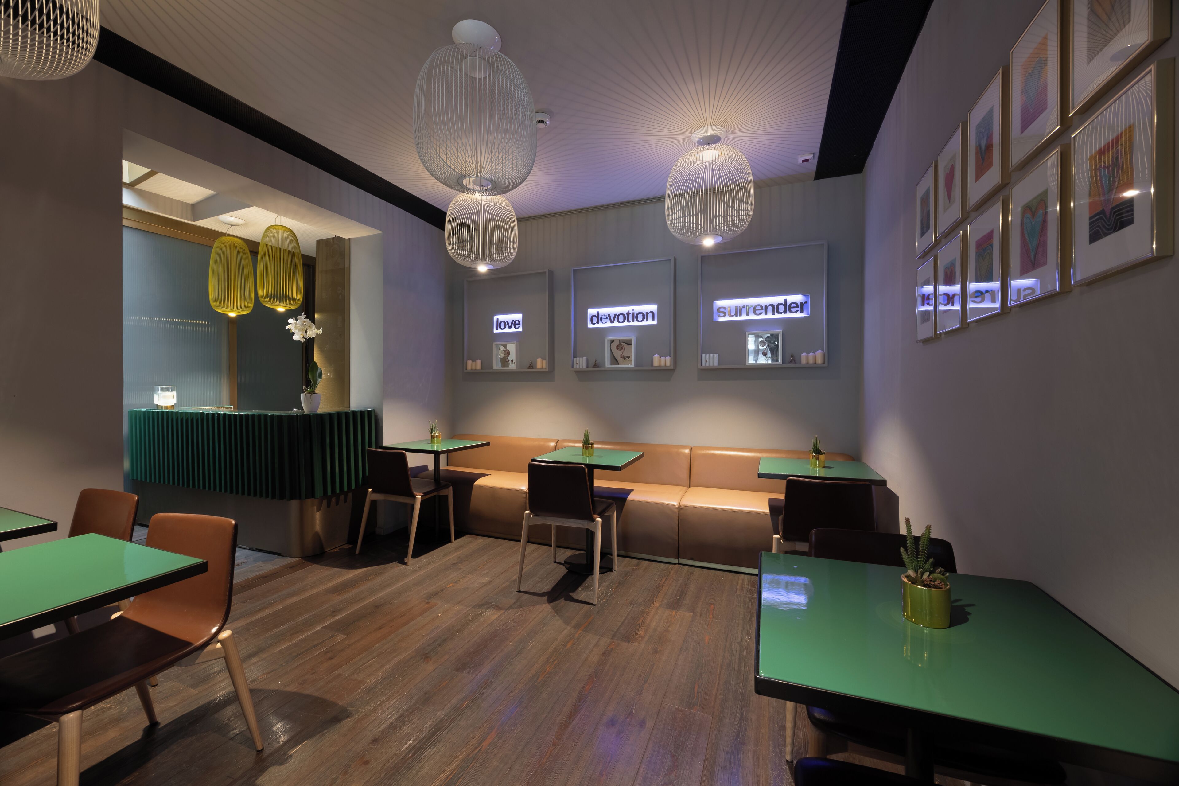 A modern restaurant interior with booths, green tables, and pendant lighting.