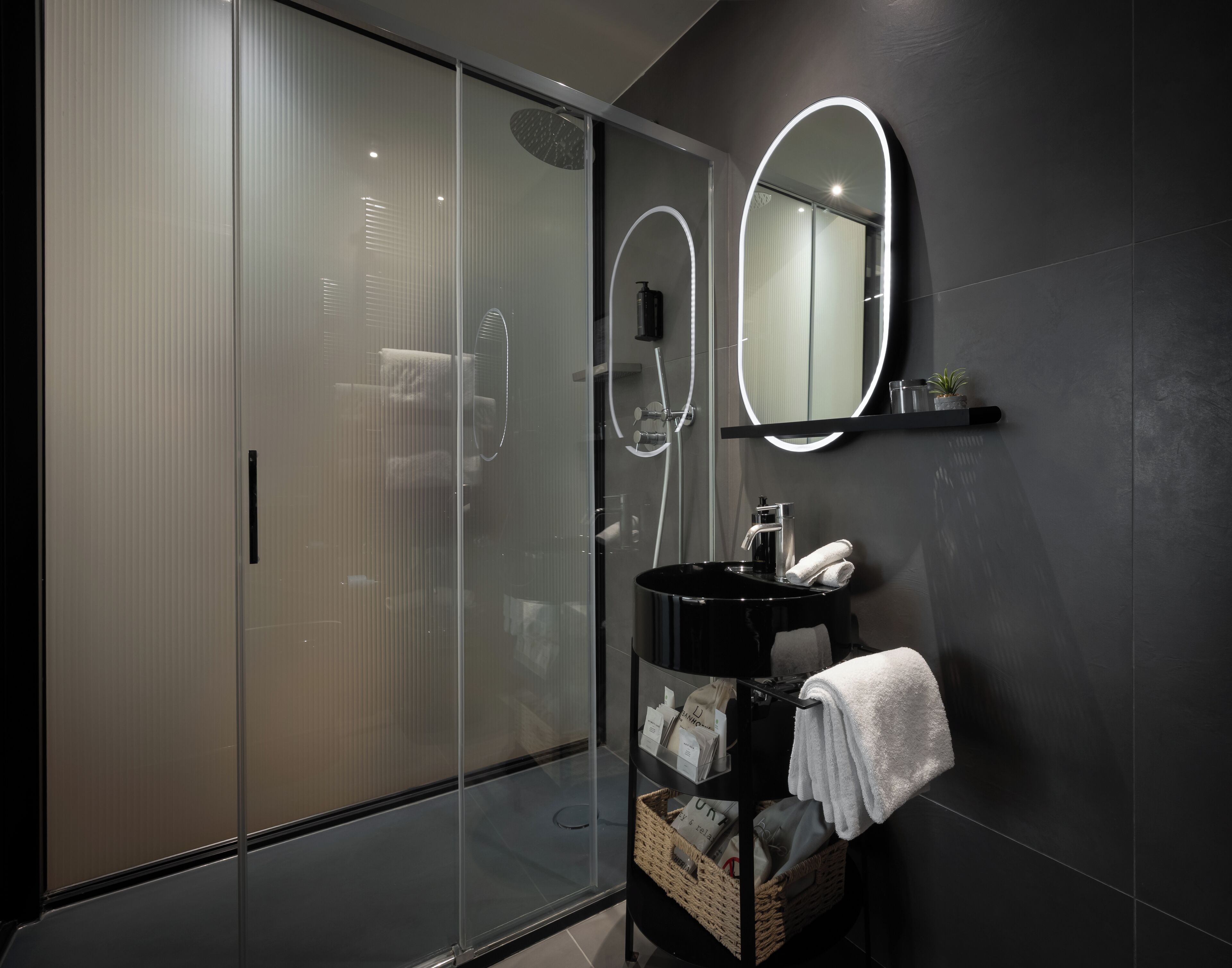 Ein modernes Badezimmer mit Duschkabine aus Glas, einem schwarzen Waschbecken mit Spiegel und einem Handtuchhalter.