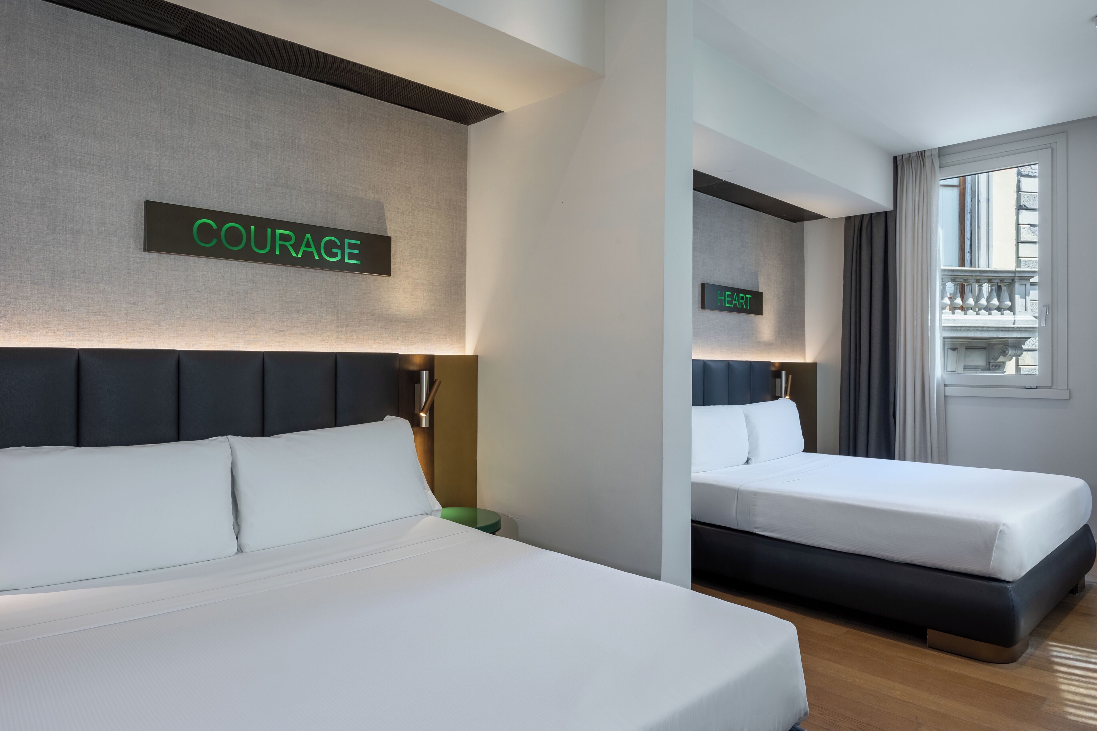 A hotel room with two beds, a sign reading "COURAGE," and a view of a balcony.