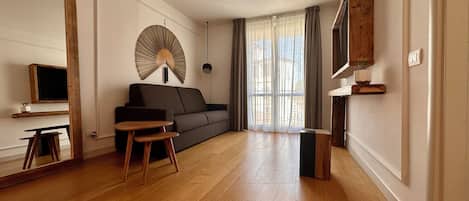 A modern living room with a sofa, a small wooden table, a fan, and a TV.