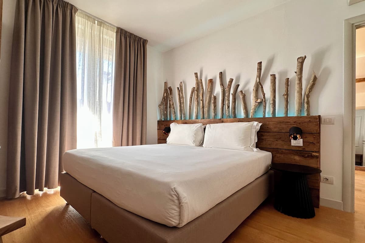 A large bed with a wooden headboard, a wooden floor, and a window with curtains.