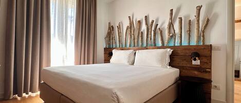 A large bed with a wooden headboard, a wooden floor, and a window with curtains.