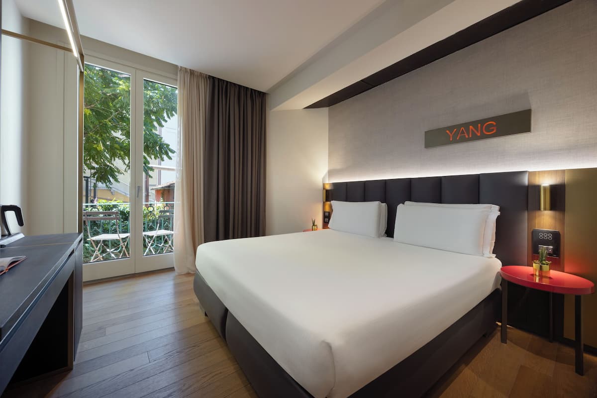 A hotel room with a large bed, a desk, a chair, and a view of the outdoors.