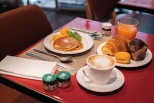 En morgenmadsopsætning med pandekager, frugt, croissanter og en kop kaffe på et bord.