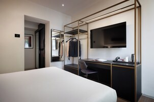 Una camera d'albergo con un letto, una scrivania, una sedia, una televisione e un armadio.