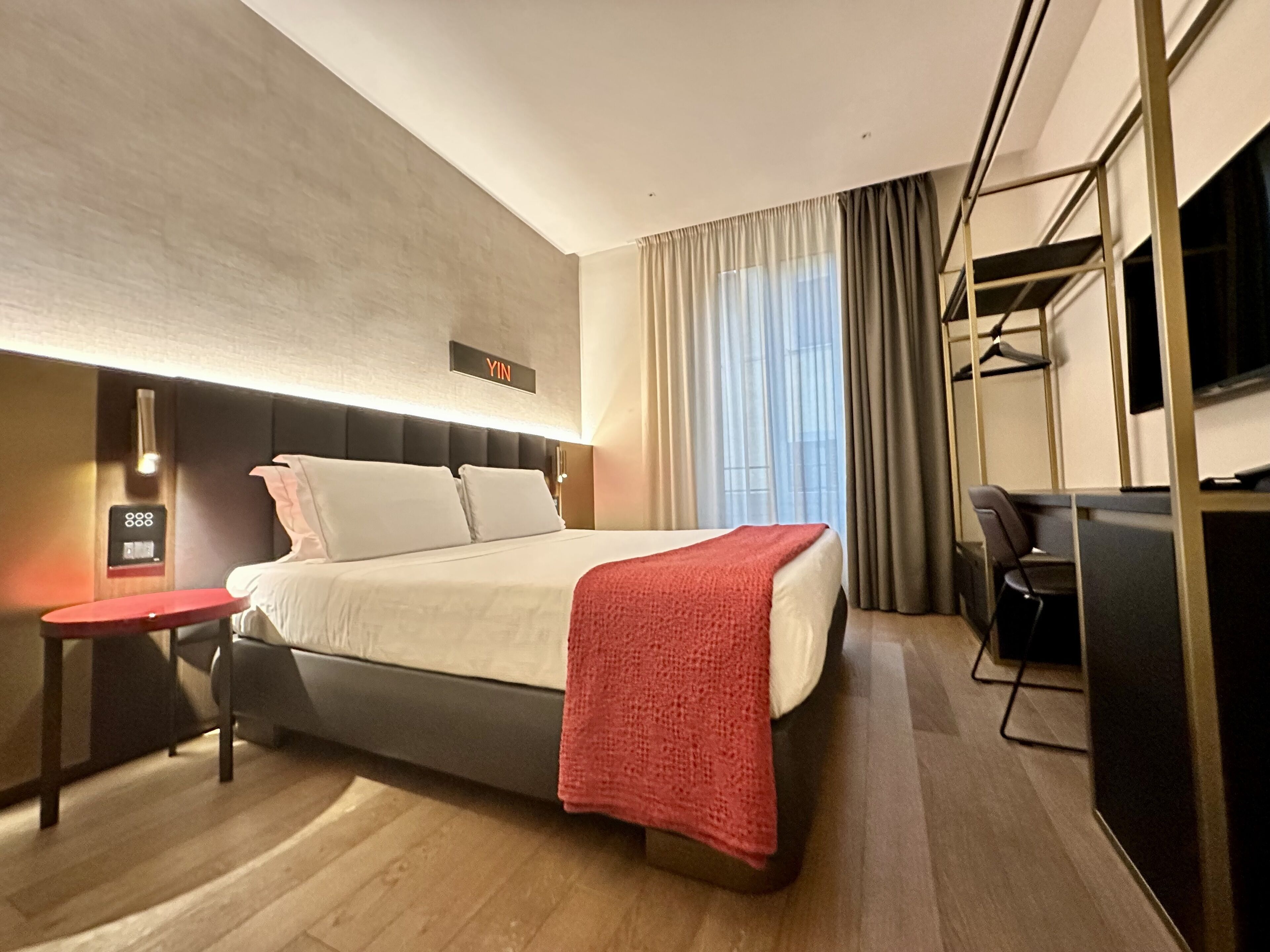 Una habitación de hotel moderna con cama, mesita de noche y televisor.