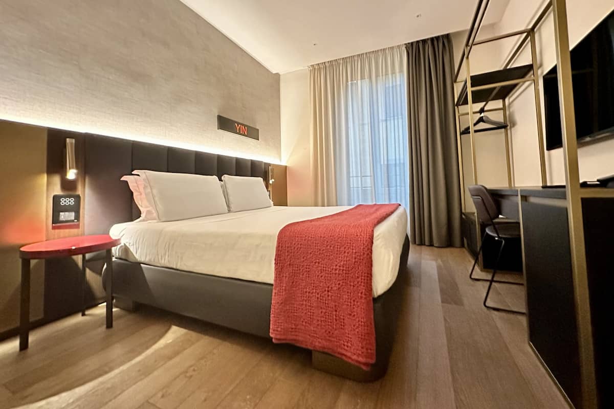 Una habitación de hotel moderna con cama, mesita de noche y televisor.