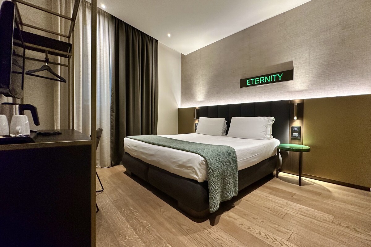 A modern hotel room with a bed, a desk with a coffee maker, and a sign reading 'ETERNITY'.