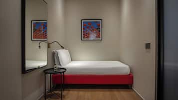 Una habitación pequeña y moderna con una cama individual, una mesita de noche y un espejo.