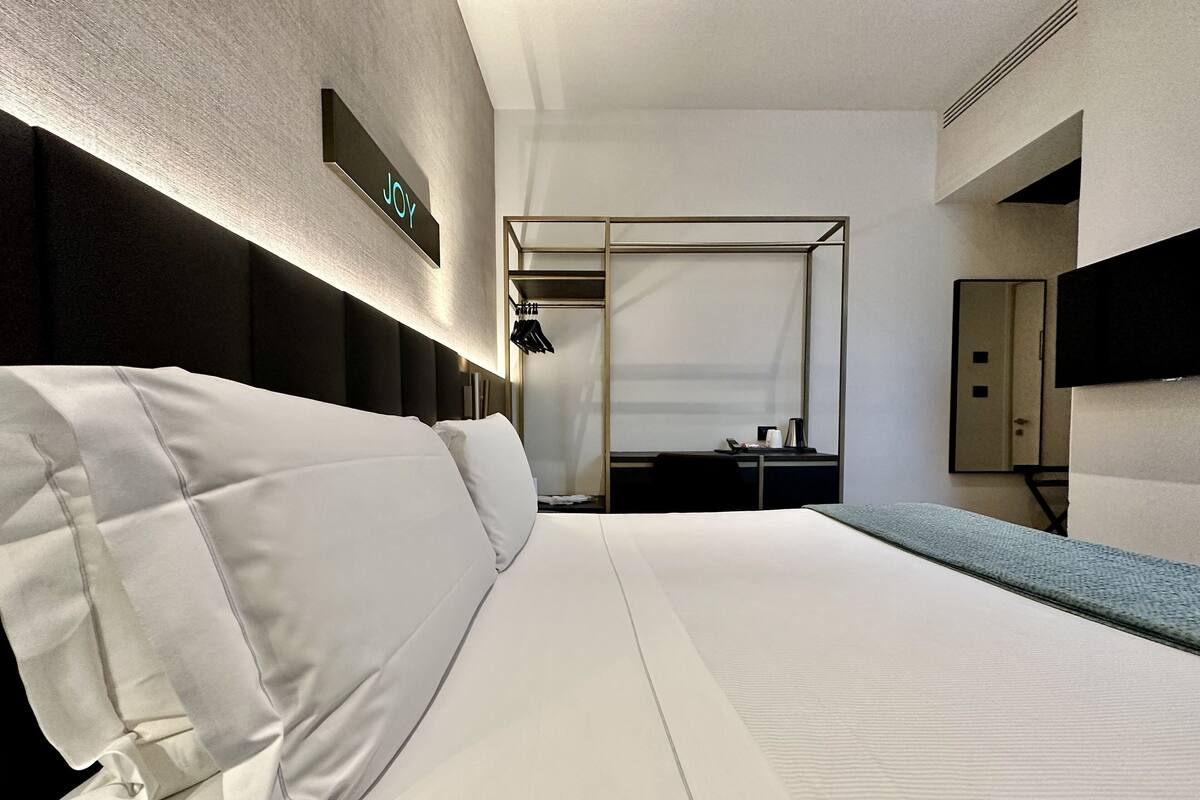 Habitación de hotel con cama, escritorio, silla, televisor y armario.