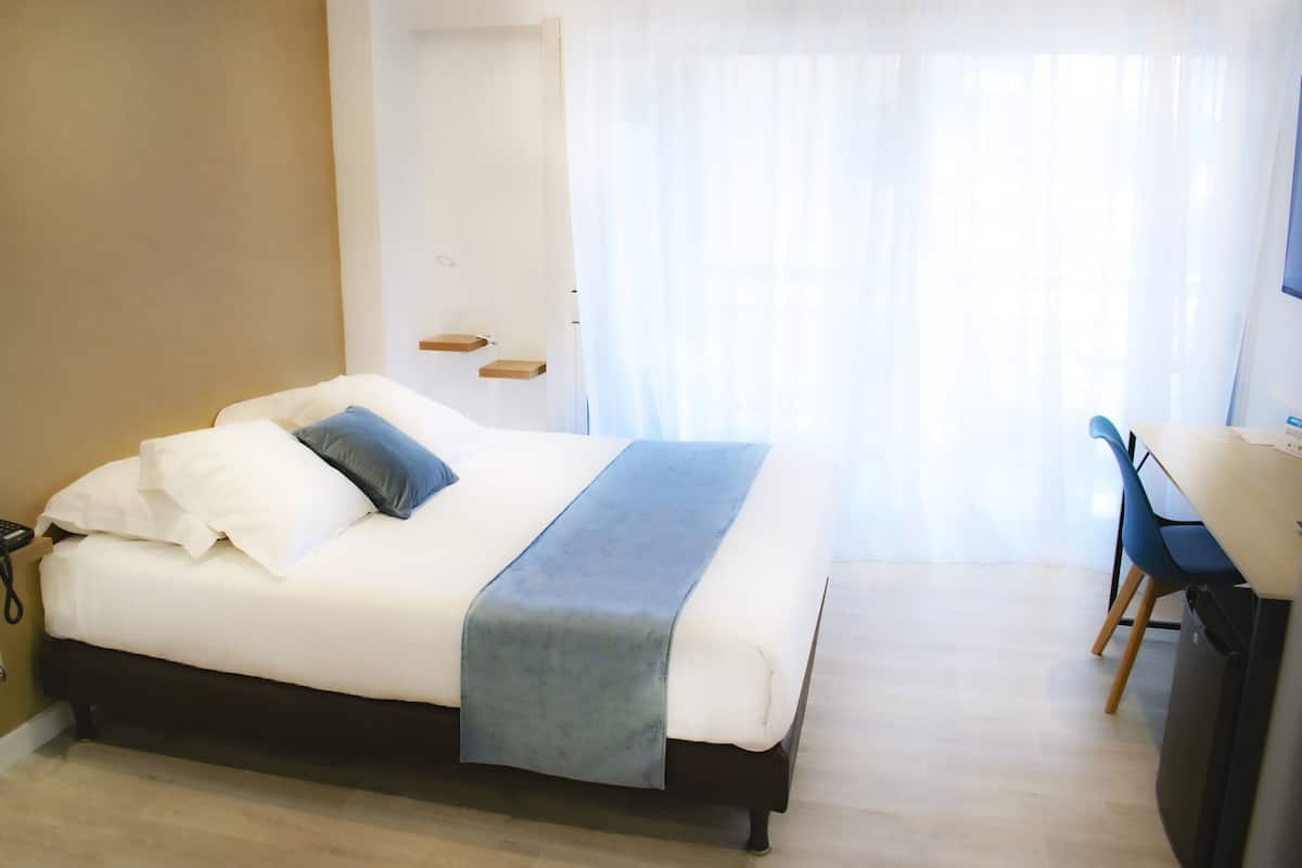 A neatly arranged bedroom with a bed, bedside tables, a desk, and a chair.