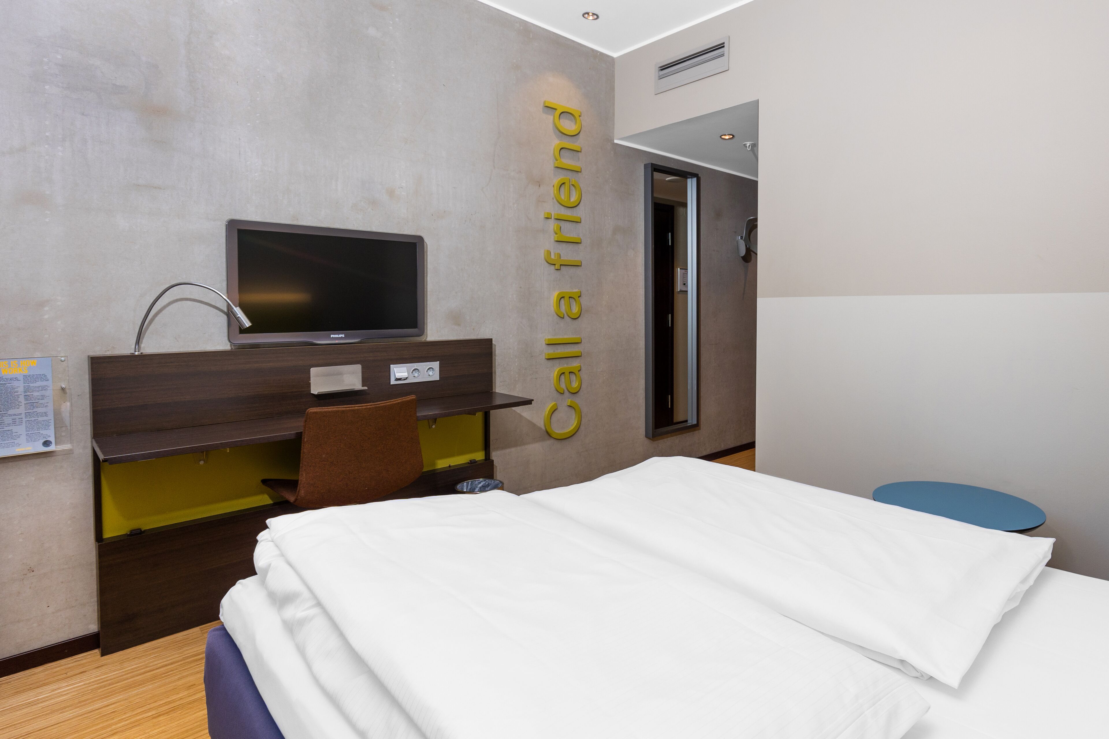 Habitación de hotel con cama, escritorio, televisor de pantalla plana, espejo y puerta.