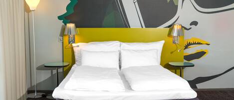 Una cama doble con sábanas blancas, cabecera marrón y dos lámparas de noche.