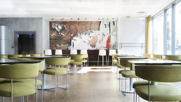 A modern dining area with green chairs and tables, a large abstract painting on the wall, and a view of the city through large windows. - Comfort Hotel Kristiansand (Kristiansand)