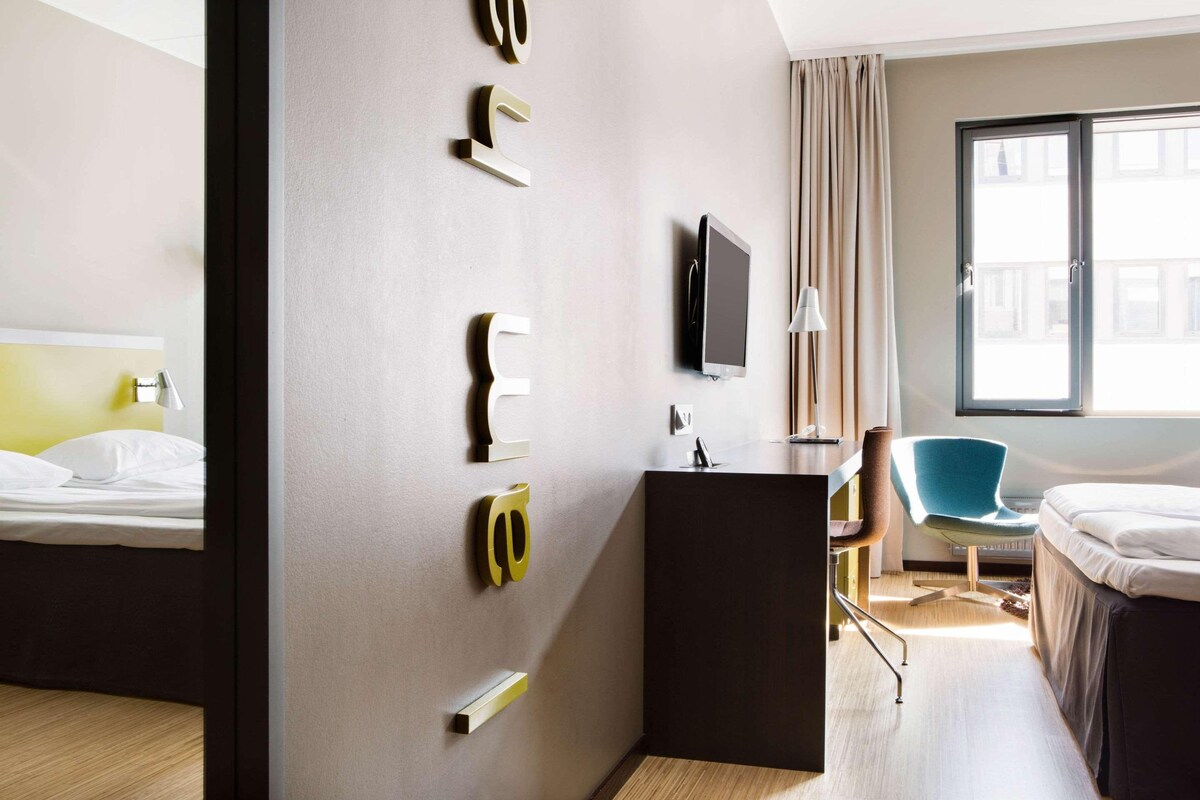 A hotel room with a bed, a desk, a chair, and a TV mounted on the wall.