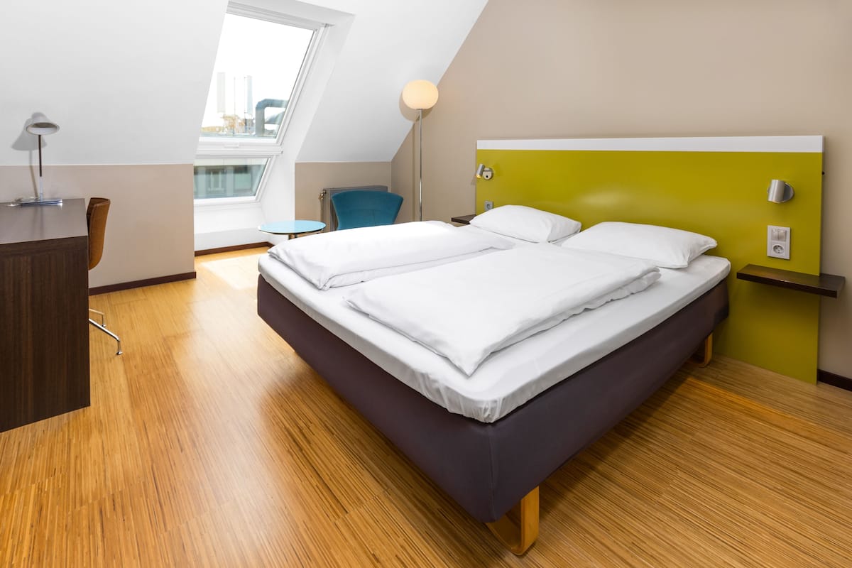 Habitación de hotel moderna con cama, escritorio, silla y vistas a través de un tragaluz.