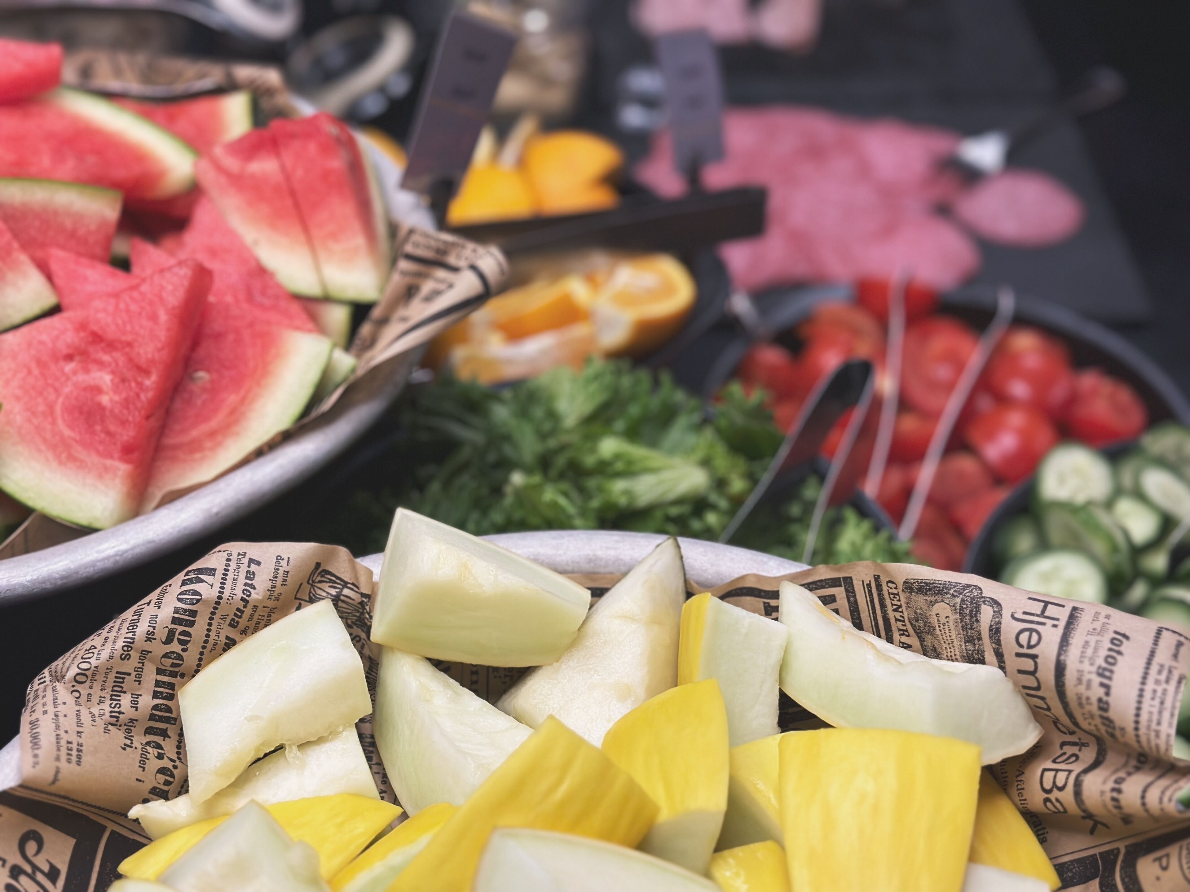 Variedad de frutas y verduras frescas exhibidas en bandejas forradas con periódico.
