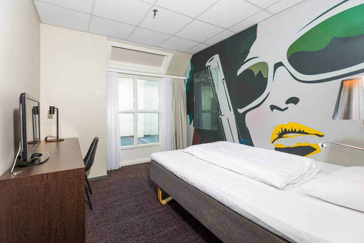 Una habitación de hotel con cama, escritorio, silla y un amplio ventanal.