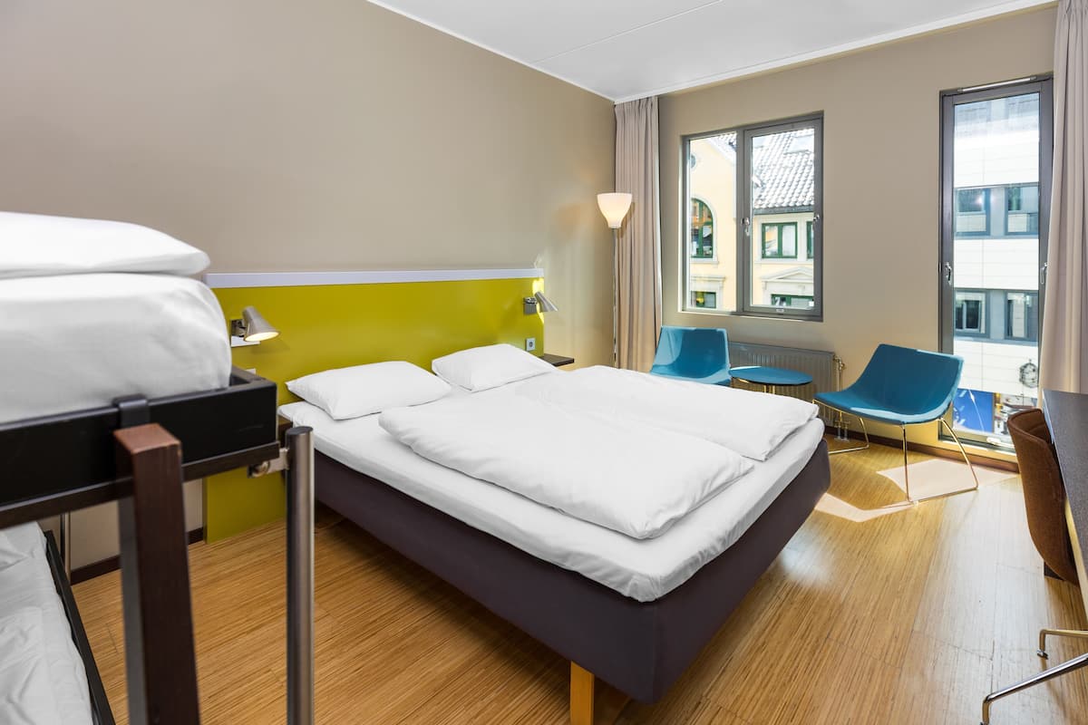 Habitación de hotel con cama, escritorio, silla y ventana con vistas a edificios.