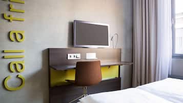 Een hotelkamer met een bed, een bureau met stoel, een televisie en een bedieningspaneel aan de muur.