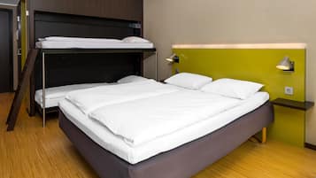 Una habitación con literas, una cama individual, una mesita de noche con lámpara y un enchufe.