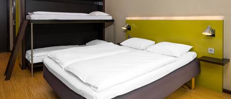A room with a bunk bed, a single bed, a bedside table with a lamp, and a wall socket.