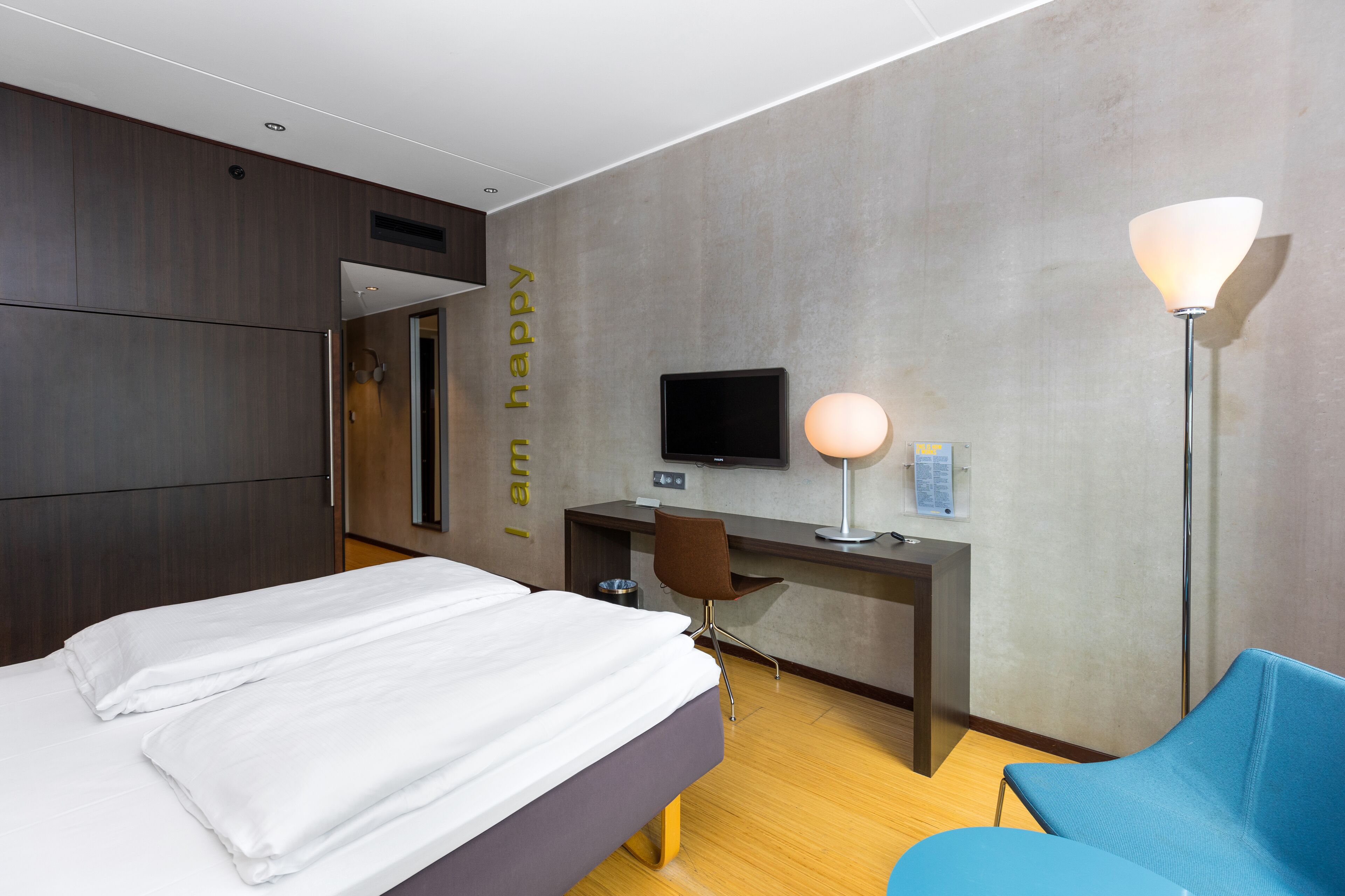 Et moderne hotelværelse med seng, skrivebord, stol, fjernsyn og lampe.