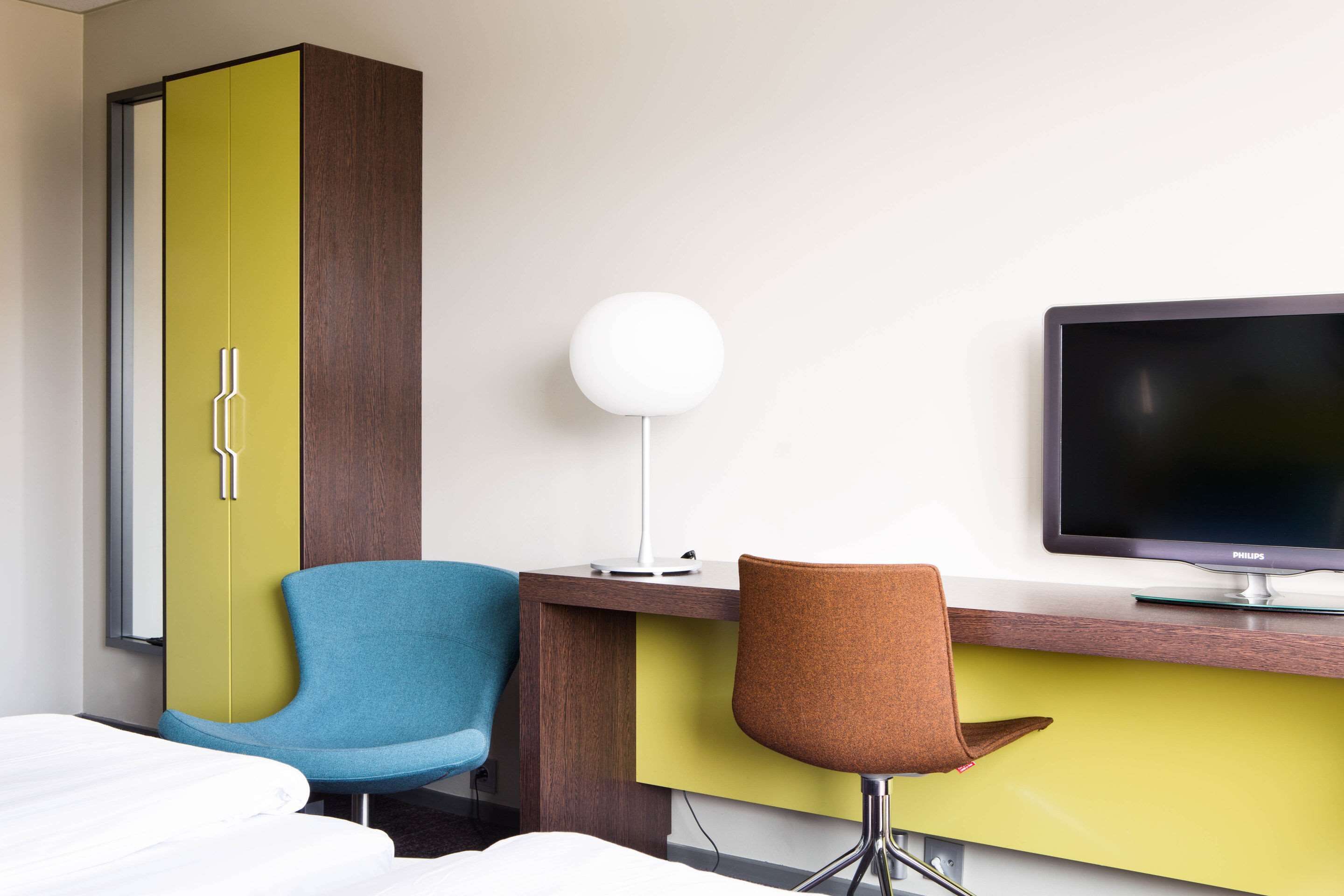 Una habitación de hotel con una cama, un escritorio con computadora, un televisor y dos sillas.