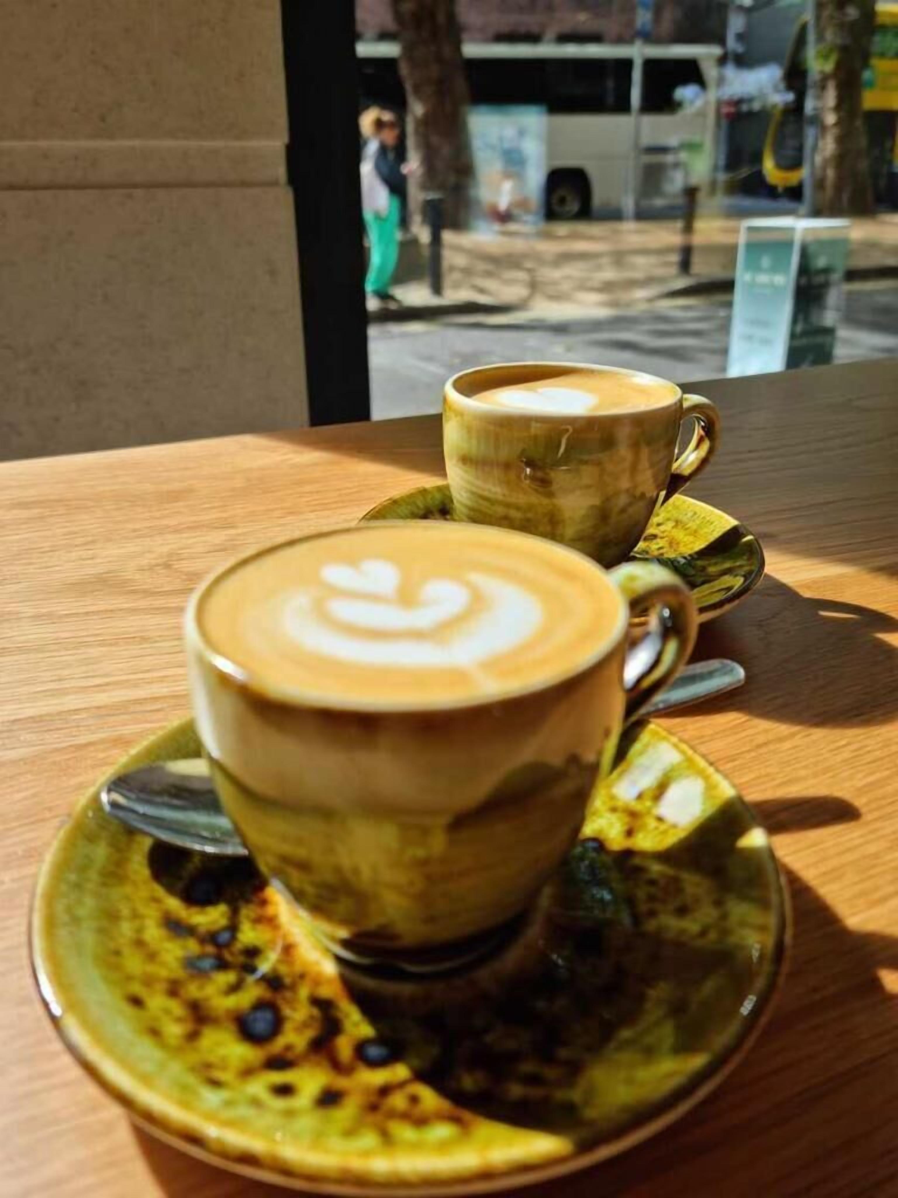 Two cups of coffee on a wooden table with a green saucer.