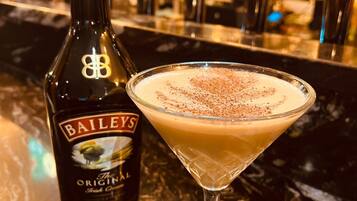 A bottle of Bailey's Original Irish Cream and a martini glass with a frothy drink on a bar counter.