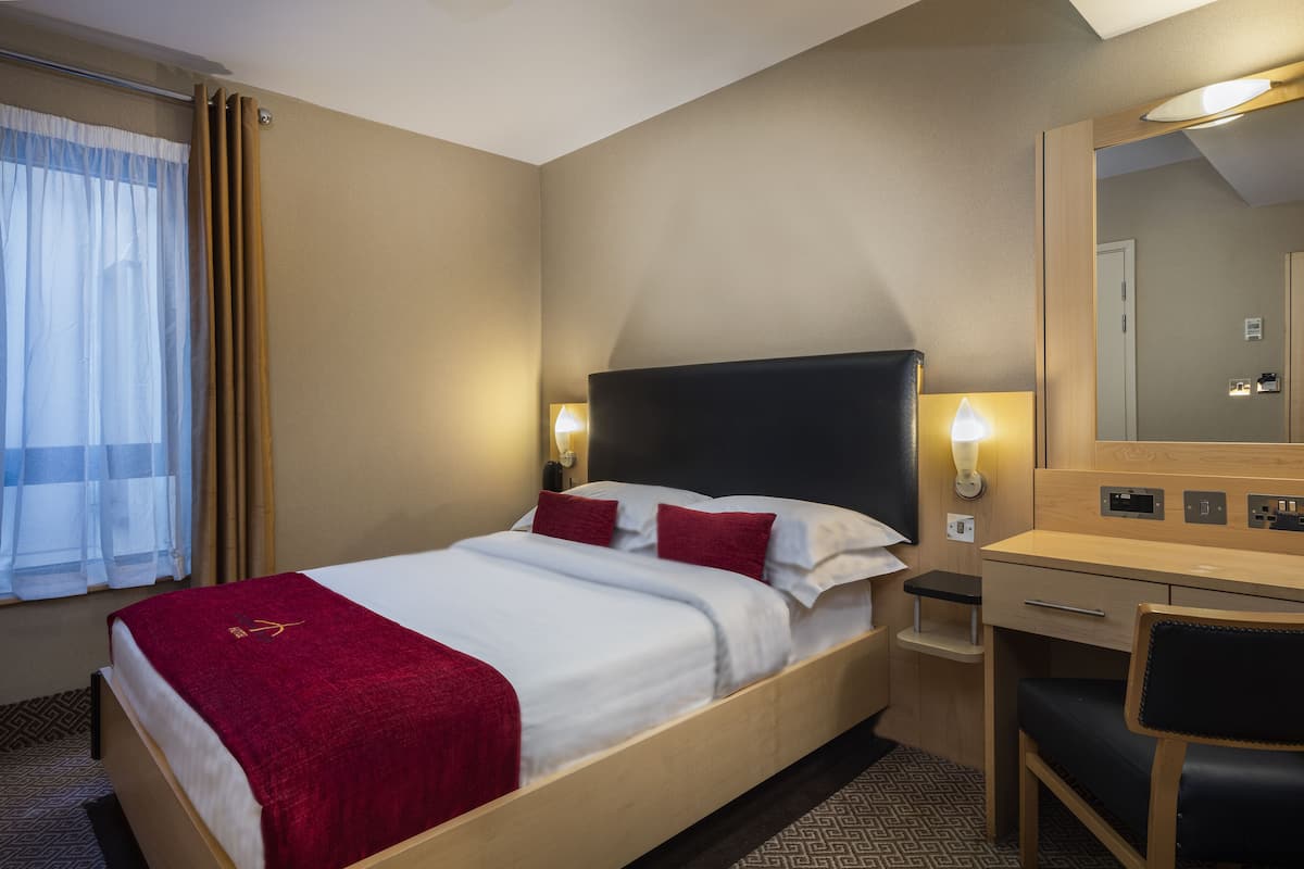 A hotel room with a bed, bedside tables, a desk, and a chair.