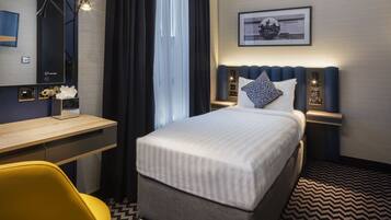 Ein Hotelzimmer mit Bett, Schreibtisch, Sessel, Nachttisch und Wandlampe.