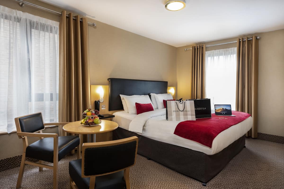 A hotel room with a bed, a desk, a chair, a table with fruit, and a laptop.