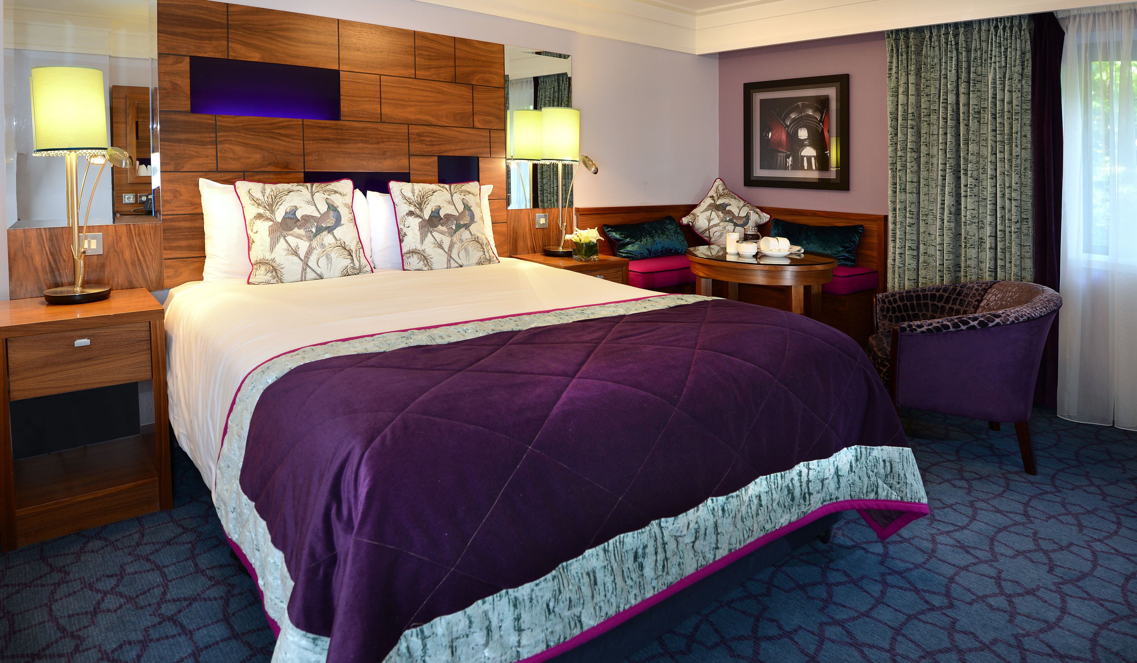 Ein Hotelzimmer mit einem großen Bett, einem Nachttisch, einem Sessel und einem kleinen Tisch mit Lampe.