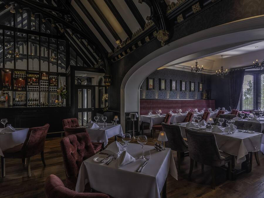 Ein Restaurant mit mehreren Esstischen, einer Bar mit Flaschenregalen und einer gewölbten Decke mit aufwendigen Holzarbeiten.