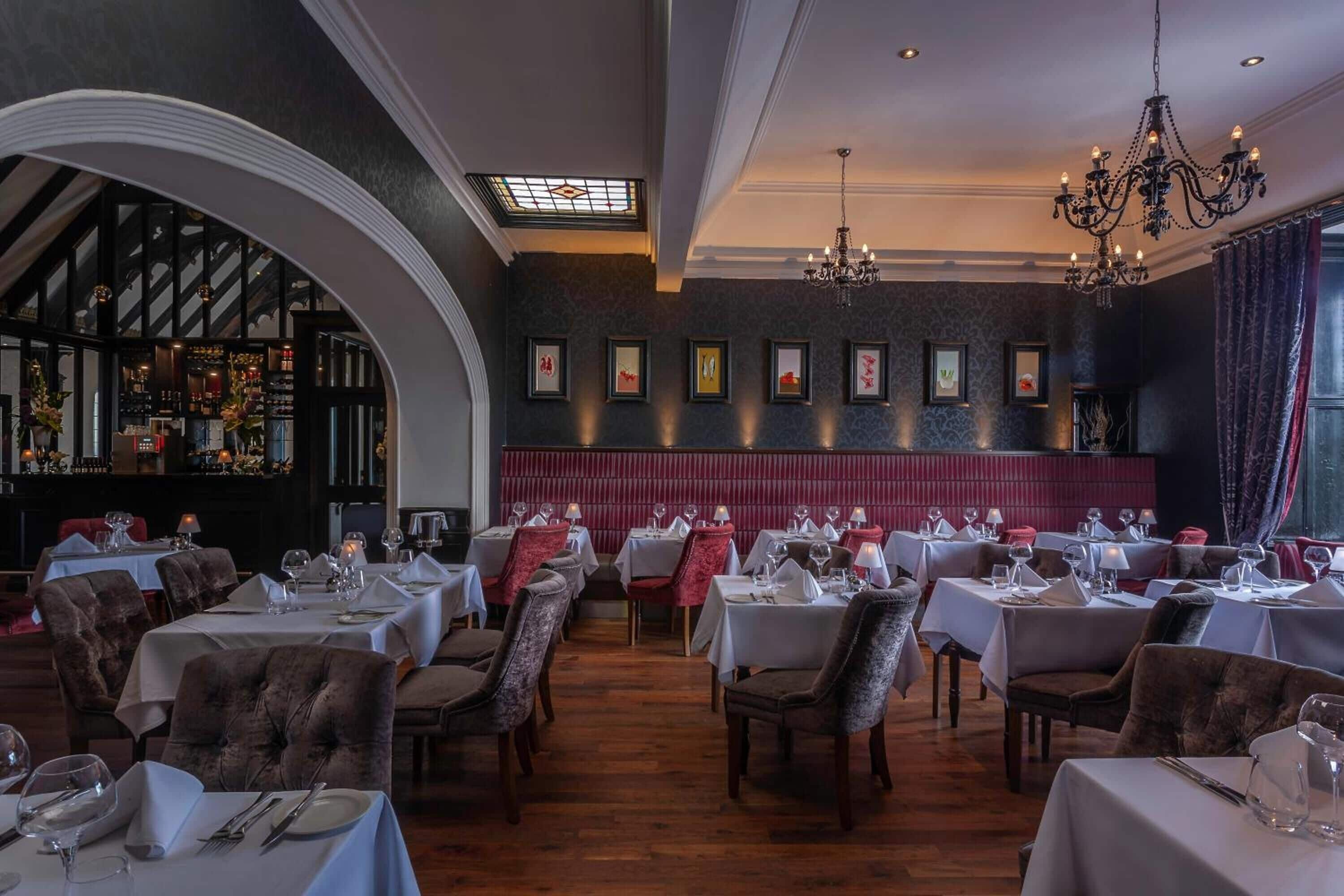 Un restaurante con varias mesas dispuestas para comer, una araña y obras enmarcadas en las paredes.