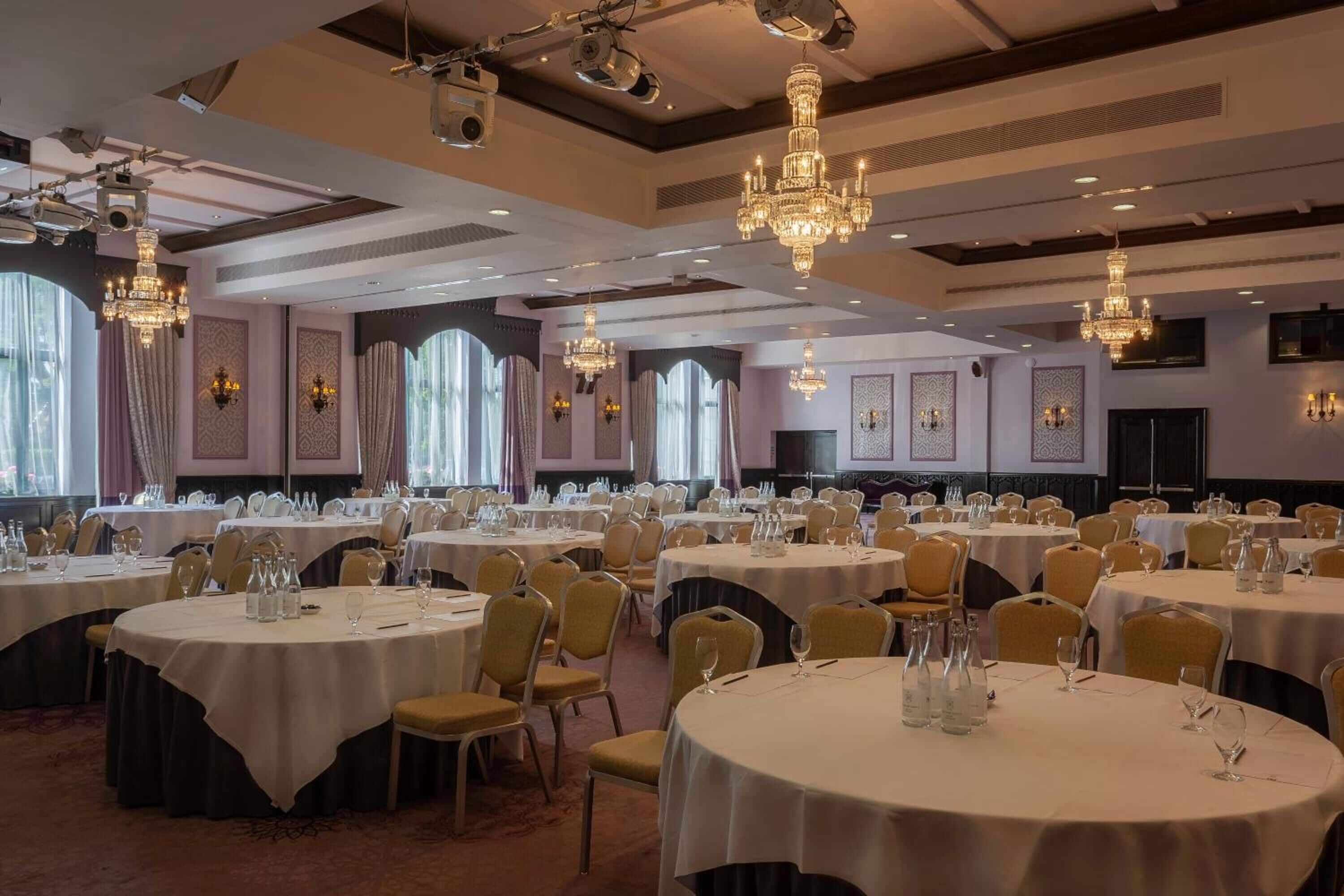 A banquet hall with round tables, chandeliers, and wall sconces.