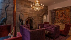 Una habitación con pared de piedra, un candelabro grande y un tapiz.