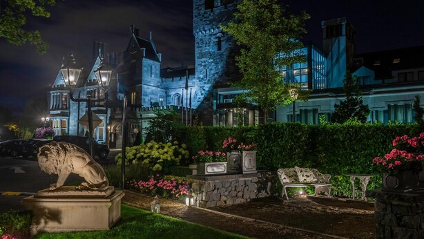 Un edificio histórico con una torre destacada y arquitectura tradicional, rodeado de jardines cuidados y una estatua.