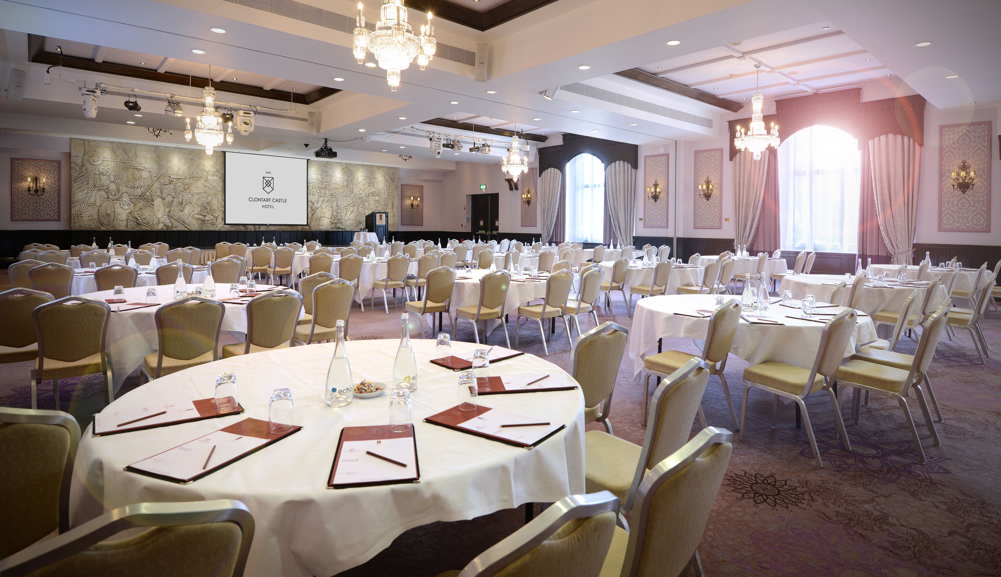 A large conference room with round tables, chairs, and a projector screen.