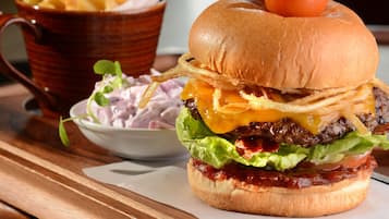 A burger with a pickle on top, served with fries and a side salad on a wooden table.
