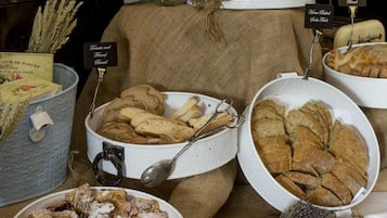 Une table de buffet proposant une variété de produits de boulangerie, notamment du pain, des muffins et des pâtisseries, disposés sur une table recouverte d’une toile de jute.