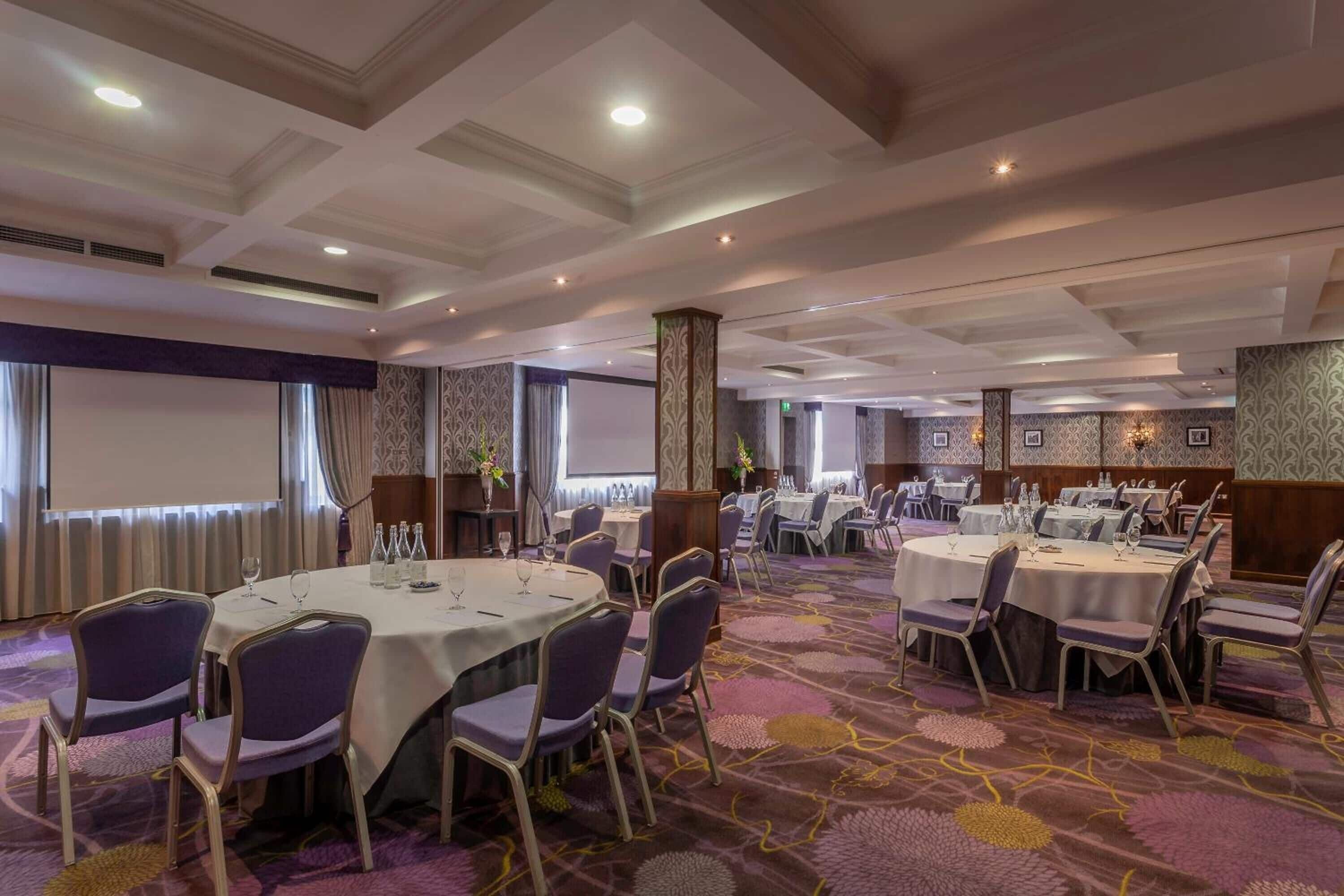 Un salón de conferencias con mesas redondas, sillas y una pantalla para proyector.