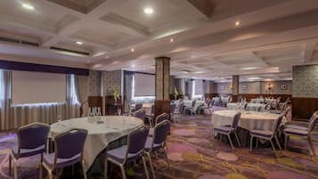 Un salón de conferencias con mesas redondas, sillas y una pantalla para proyector.