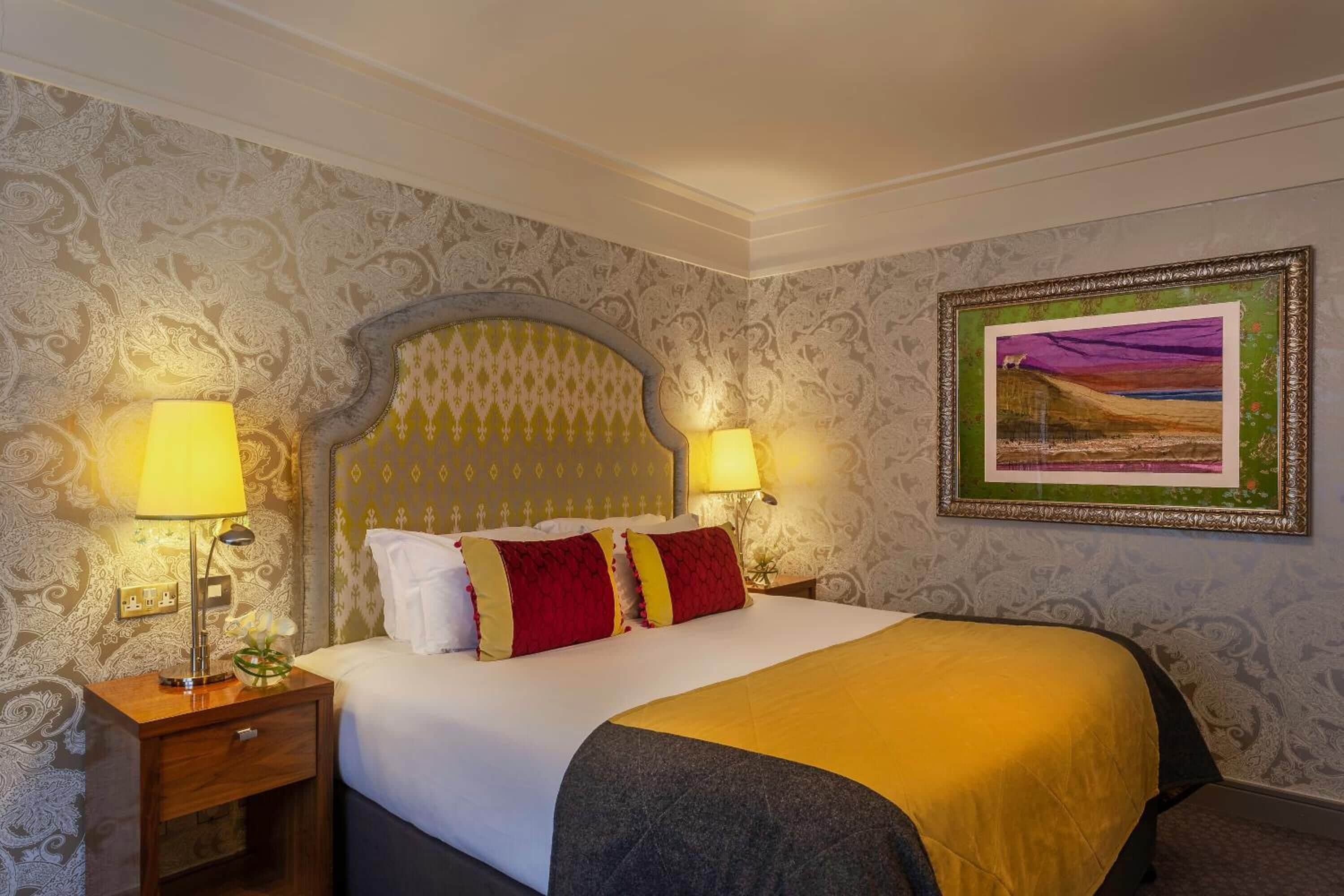 Una habitación de hotel con una cama grande, dos lámparas de noche, una mesita de noche y un cuadro enmarcado en la pared.