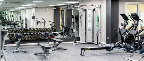 A gym with various exercise equipment, including treadmills, weight machines, and a bench.